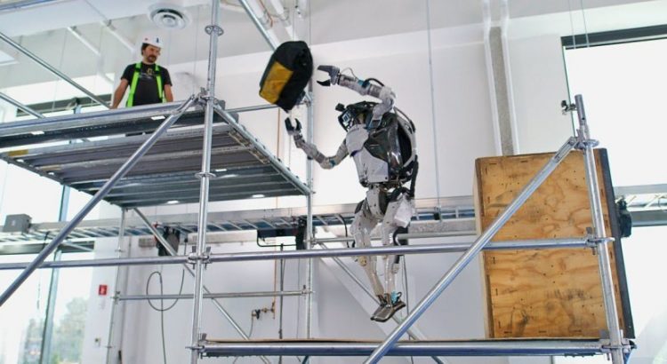 Le robot humanoide Atlas en train de lancer un sac d’outils a un ouvrier sur un echaffaudage
