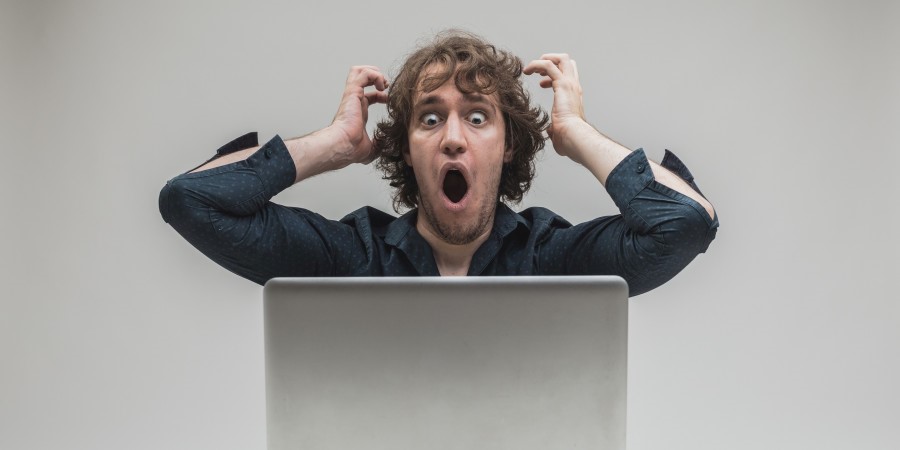 Un homme tres surpris devant son ordinateur, les mains en l’air et la bouche grand ouvert 