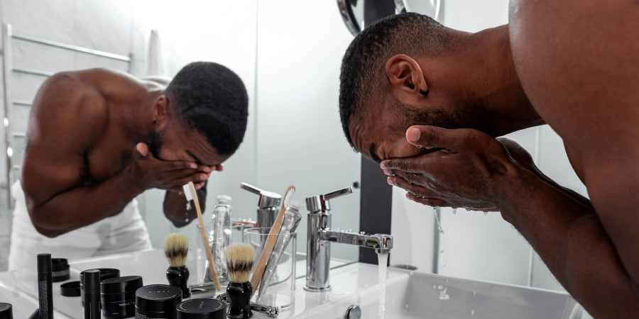 Un homme en train de se laver le visage devant le miroir 