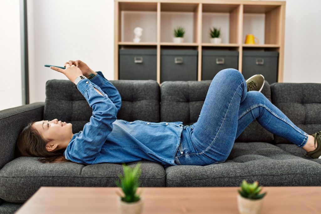 Une femme allongee sur le sofa en train de naviguer sur son smartphone 