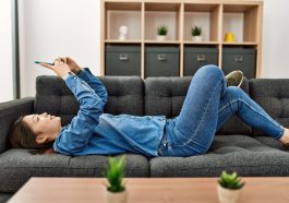 Une femme allongee sur le sofa en train de naviguer sur son smartphone