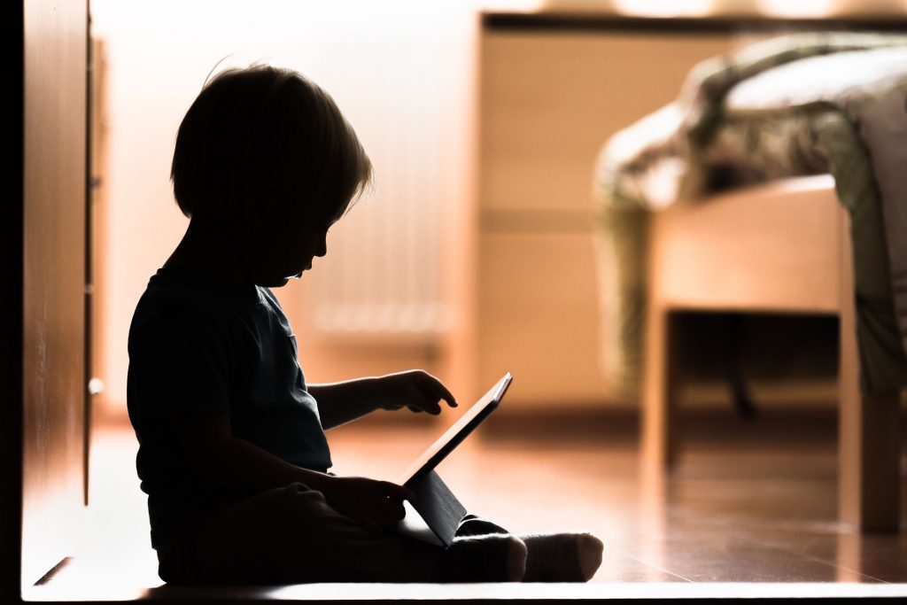 Silhouette d’un bébé assis par terre en train de scroller un tablette numérique 