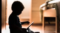 Silhouette d’un bébé assis par terre en train de scroller un tablette numérique