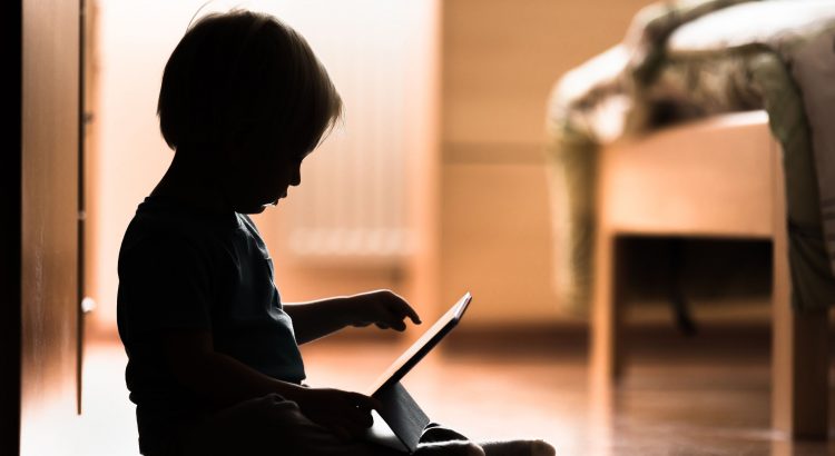 Silhouette d’un bébé assis par terre en train de scroller un tablette numérique