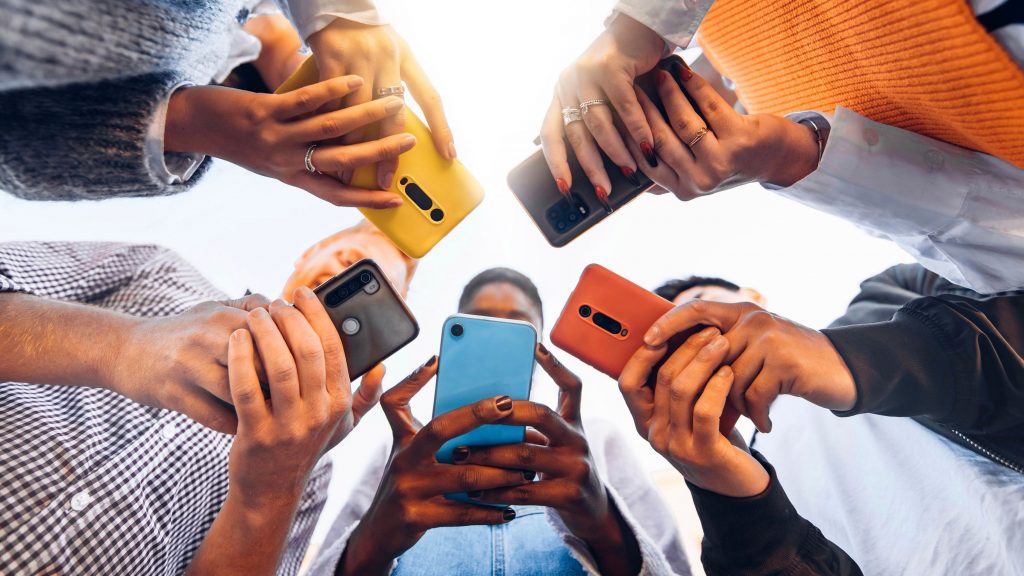 Photo prise d’en bas de cinq personnes formant un cercle et tenant leur smartphone 