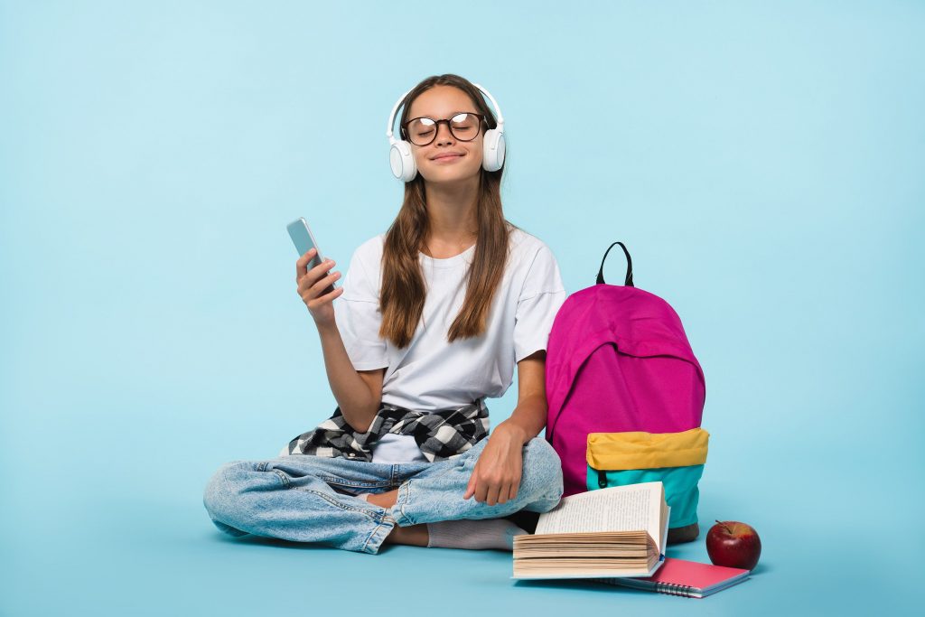 Photo sur fond bleu d’une adolescente portant un casque blanc tout en tenant son smartphone dans une autre main 