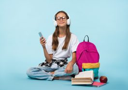 Photo sur fond bleu d’une adolescente portant un casque blanc tout en tenant son smartphone dans une autre main