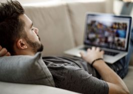 Un homme allonge sur un canape en train de manipuler un pc