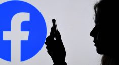 Silhouette d’un profil d’une femme regardant son smartphone devant un grand logo de Facebook