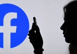 Silhouette d’un profil d’une femme regardant son smartphone devant un grand logo de Facebook