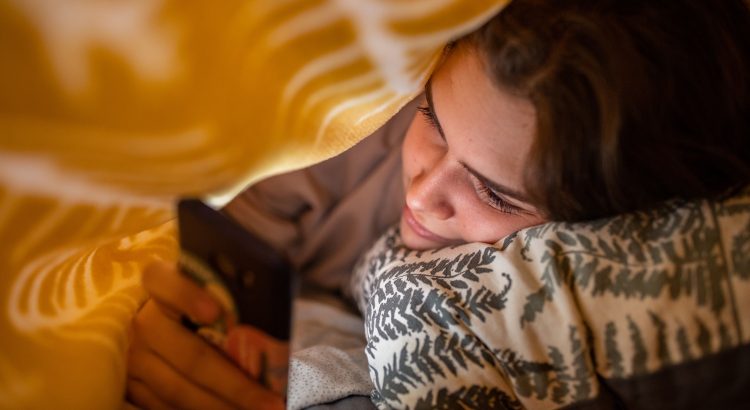 Une femme manipulant son smartphone sous une couverture