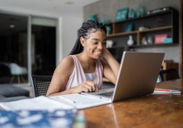 Une jeune femme souriant en train de travailler sur son ordinateur portable