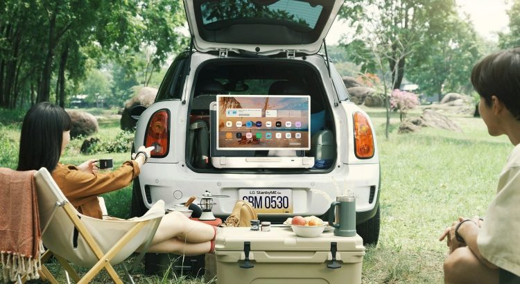 Le coffre d’une voiture ouvert sur l’ecran de television LG StanbyME Go dans la nature, deux personnes (homme et femme) regardant le tele