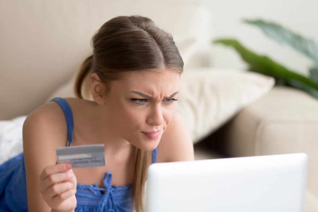Une femme fixant l’ecran d’un ordinateur, une carte bancaire a la main 