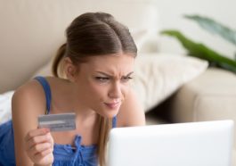 Une femme fixant l’ecran d’un ordinateur, une carte bancaire a la main