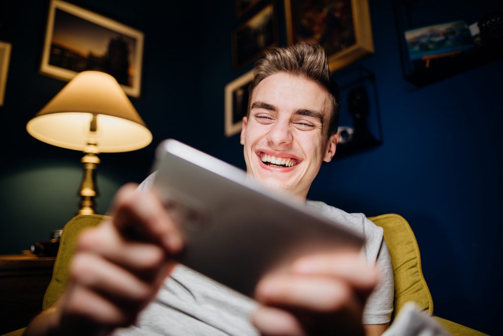 Un jeune homme riant en fixant sur sa tablette numerique 