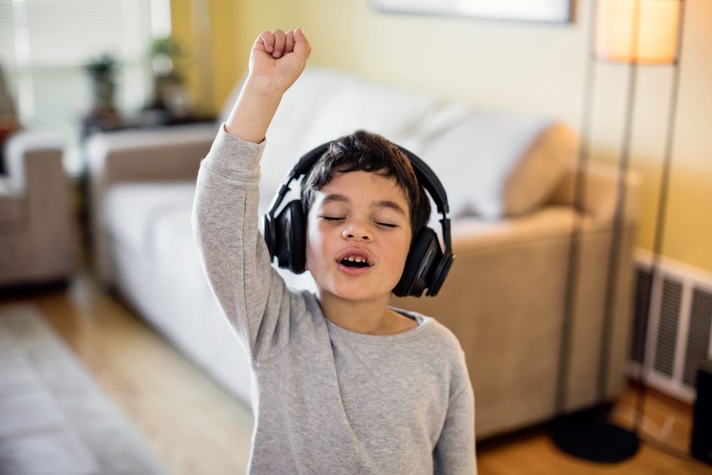 Un petit garcon ecoutant de la musique, des casques aux oreilles, fermant les yeux et levant le bras  