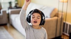Un petit garcon ecoutant de la musique, des casques aux oreilles, fermant les yeux et levant le bras