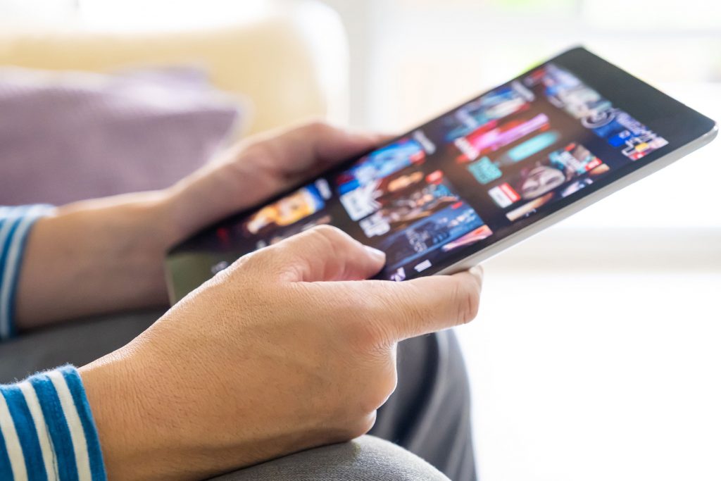 Mains d’un homme tenant une tablette numerique affichant une plateforme streaming video