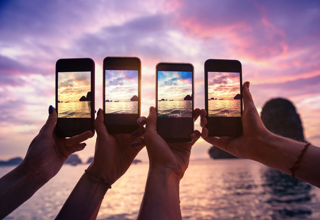 Image montrant quatre mains de personnes entrain de prendre une photo sur leur smartphone respectif