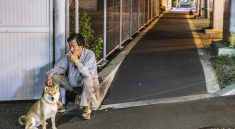 Un vieil homme asiatique assis au bord de la route, fumant une cigarette et tenant la laisse de son chien