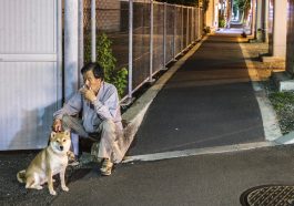 Un vieil homme asiatique assis au bord de la route, fumant une cigarette et tenant la laisse de son chien