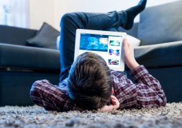 Un garcon allonge sur le tapis en train de visionner une video sur sa tablette