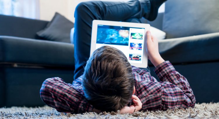 Un garcon allonge sur le tapis en train de visionner une video sur sa tablette